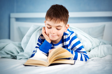 boy lying in bed with a book. child reading