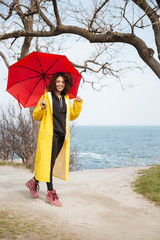 Smiling african curly young lady wearing yellow coat holding umbrella