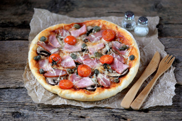 Homemade pizza with smoked meat, ham, mushrooms, cherry tomato, capers and cheese.