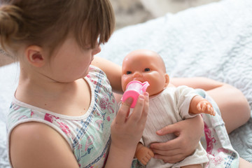 Kid girl playing with doll, feeding doll bottle