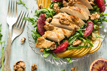 Fresh spring salad with grilled chicken breast, arugula, pear and orange slices and walnuts on wooden table. Selective focus