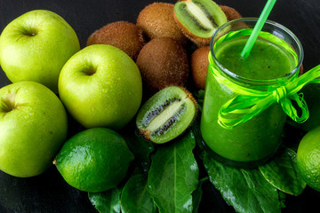 Green smoothie near ingredients for it on black wooden background. Apple, lime, spinach, kiwi. Detox. Healthy drink.