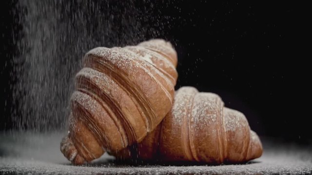 Powdered sugar sprinkling onto croissant on black background