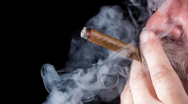 A man smokes a cigar against black background
