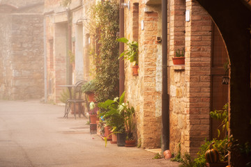 Fototapeta na wymiar Empty street of small Tuscany town San Quirico d'Orcia in the morning fog, romantic travel vintage hipster european italy background