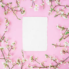 Frame of spring flowers and paper card on pink background. Flat lay, top view.