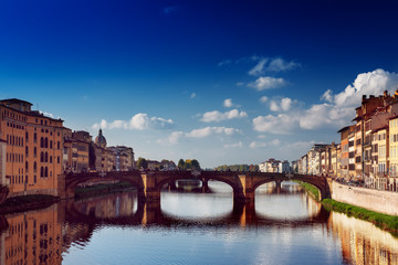 Obraz premium View from the river to the famous italian medieval bridge - Ponte Vecchio in Florence with blue sky and clouds, travel outdoor Italy sightseeing background