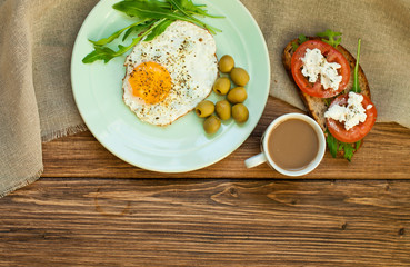 Fried eggs, a sandwich with vegetables and feta cheese and cappuccino coffee for breakfast. Tomatoes and bread on a wooden table
