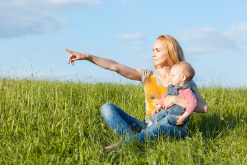 Fototapeta premium Portrait of mother and daughter in the grass. Mom points hand forward