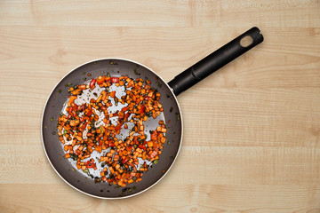Fried vegetables in a frying pan, on a light wood background