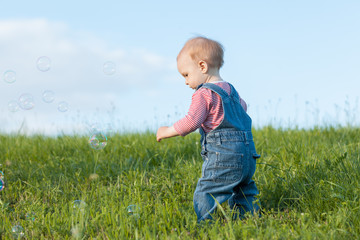 Baby walking in the grass. Around her fly soap bubbles