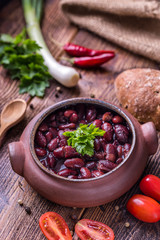 Bean soup in home crafted bowl with tomatoes on wooden table.