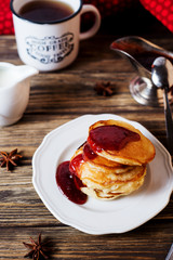 Hearty and tasty breakfast or lunch, fried pancakes with strawberry jam, milk and black tea on a dark wooden background 