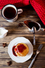 Hearty and tasty breakfast or lunch, fried pancakes with strawberry jam, milk and black tea on a dark wooden background 