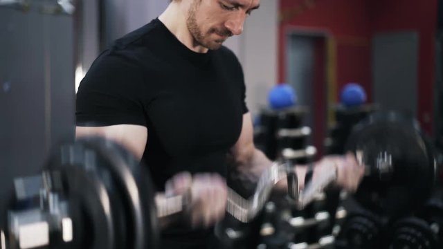 Close up of young man wearing a black T-shirt doing the last set of a barbell exercise in a gym. Handheld real time shot