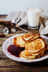Hearty and tasty breakfast or lunch, fried pancakes with strawberry jam, milk and black tea on a dark wooden background 