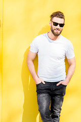 Colorful portrait of a handsome man dressed in white t-shirt and jeans on the yellow background