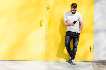 Fototapeta na wymiar Colorful portrait of a handsome man dressed in white t-shirt and jeans with phone on the yellow background