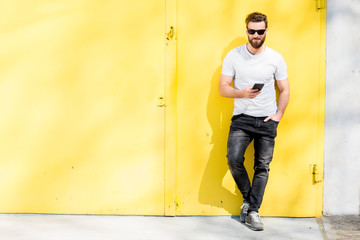 Fototapeta na wymiar Colorful portrait of a handsome man dressed in white t-shirt and jeans with phone on the yellow background