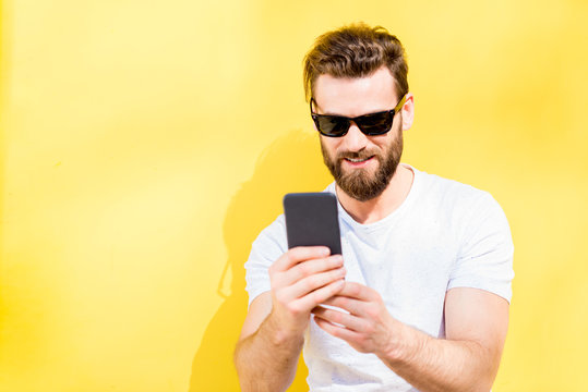 Colorful portrait of a handsome man dressed in white t-shirt using phone on the yellow background