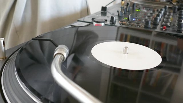 Footage of a DJ practicing mixing music on an audio mixer at home, a rotating vinyl is beside the mixer...