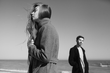 Young hipster couple posing near the sea in spring sunny day wearing trendy coats. Relationships between couple man and woman.