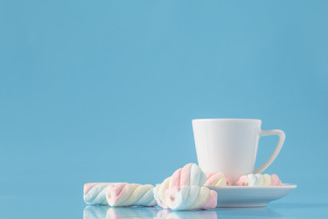 Cup of espresso coffee and twisted american marshmallow on blue