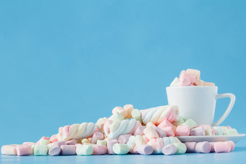 Pastel marshmallow in a white cup on a blue background. Sweet unhealthy food. Minimalism style