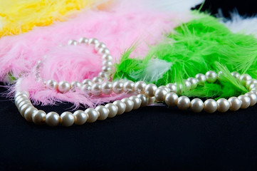 White necklace lay on black fabric in heap of colored feathers