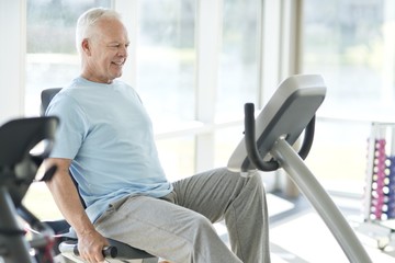 Senior man exercising on stationary bicycle indoors