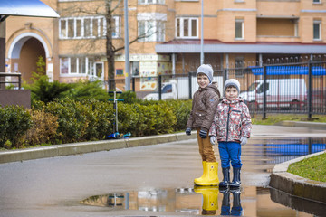 Obraz na płótnie Canvas Two little boys, squat on a puddle, with little umbrellas