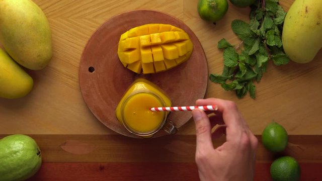 man puts a cocktail tube and a leaf of mint into a glass of Juicy mango smoothie. Fresh drinks. Healthy life concept