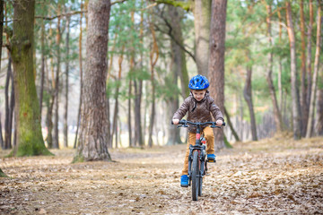 Happy kid boy of 3 or 5 years having fun in autumn forest with a bicycle on beautiful fall day. Active child wearing bike helmet. Safety, sports, leisure with kids concept.