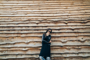 Fashionable model in sunglasses posing at the wooden wall.