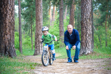 Fototapeta na wymiar Little kid boy of 3 years and his father in autumn forest with a bicycle. Dad teaching his son. Man happy about success. Child with helmet. Safety, sports, leisure with kids concept.