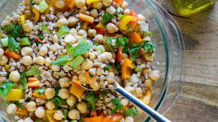 A salad consisting of farro, garbanzo beans, bell peppers, and spring onions served with olive oil on wooden table- healthy vegan eating concpet