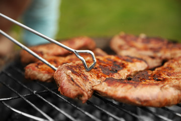 Preparing of steaks on barbecue grill in garden, close up view