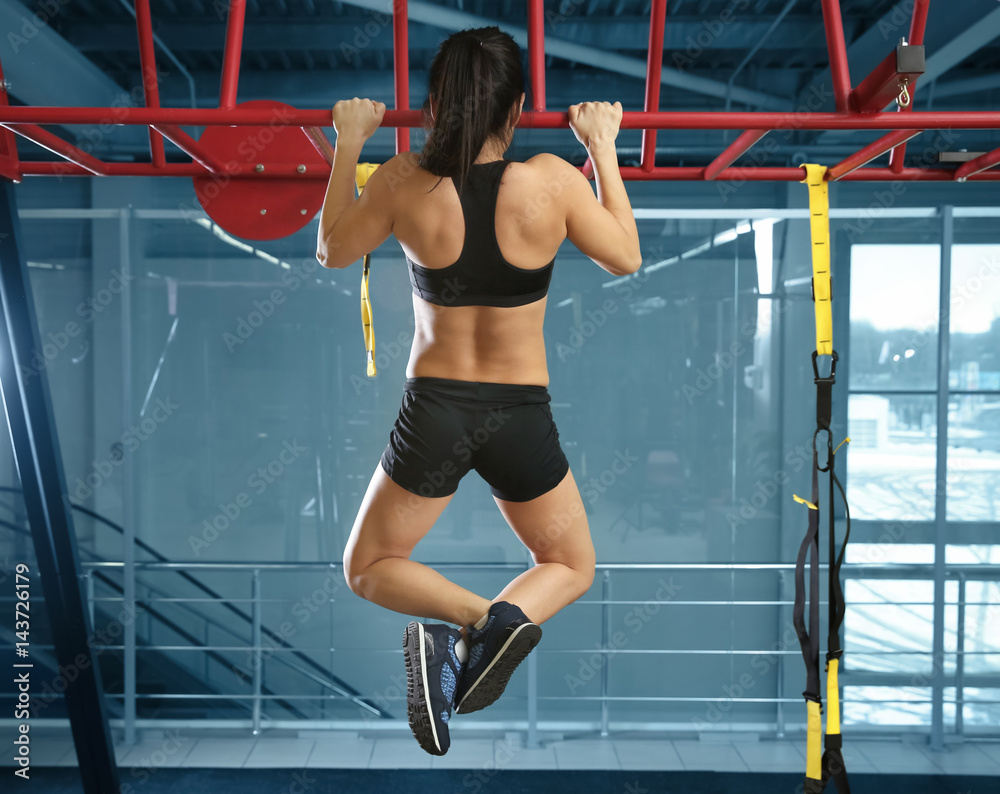 Wall mural Athletic woman training on horizontal bar in gym