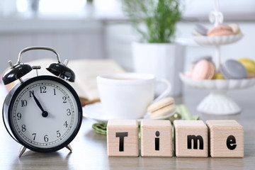 Fototapeta na wymiar Retro alarm clock showing five minutes to eleven and wooden cubes with word TIME on lunch table