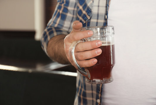 Man holding glass of beer near his big belly in pub