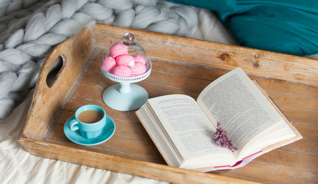 photo of stand with marshmallows, cup of coffee and book on the board on the bed