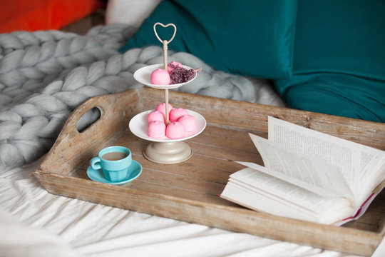 photo of stand with marshmallows and branch of lavender, cup of coffee and book on the board on the bed