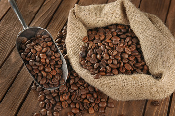Bag with coffee beans and scoop on wooden background