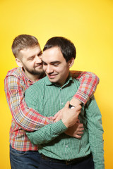 Happy gay couple posing on yellow background