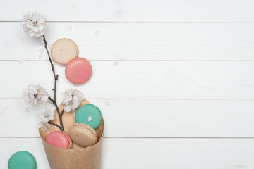 Macaroon cookies and flowers on white wooden background