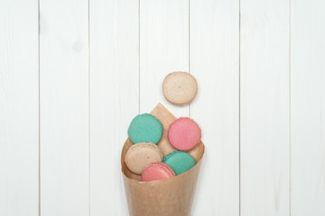 Package with colored macaroons on a white wooden background