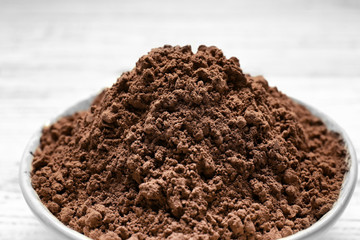 Plate with cocoa powder on white wooden background