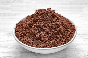 Plate with cocoa powder on white wooden background