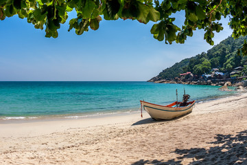 Fototapeta na wymiar A boat at the white sand beach of the tropical blue sea. Daytime, Koh Phangan, Thailand