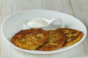 Potato pancakes on a white plate with sour cream